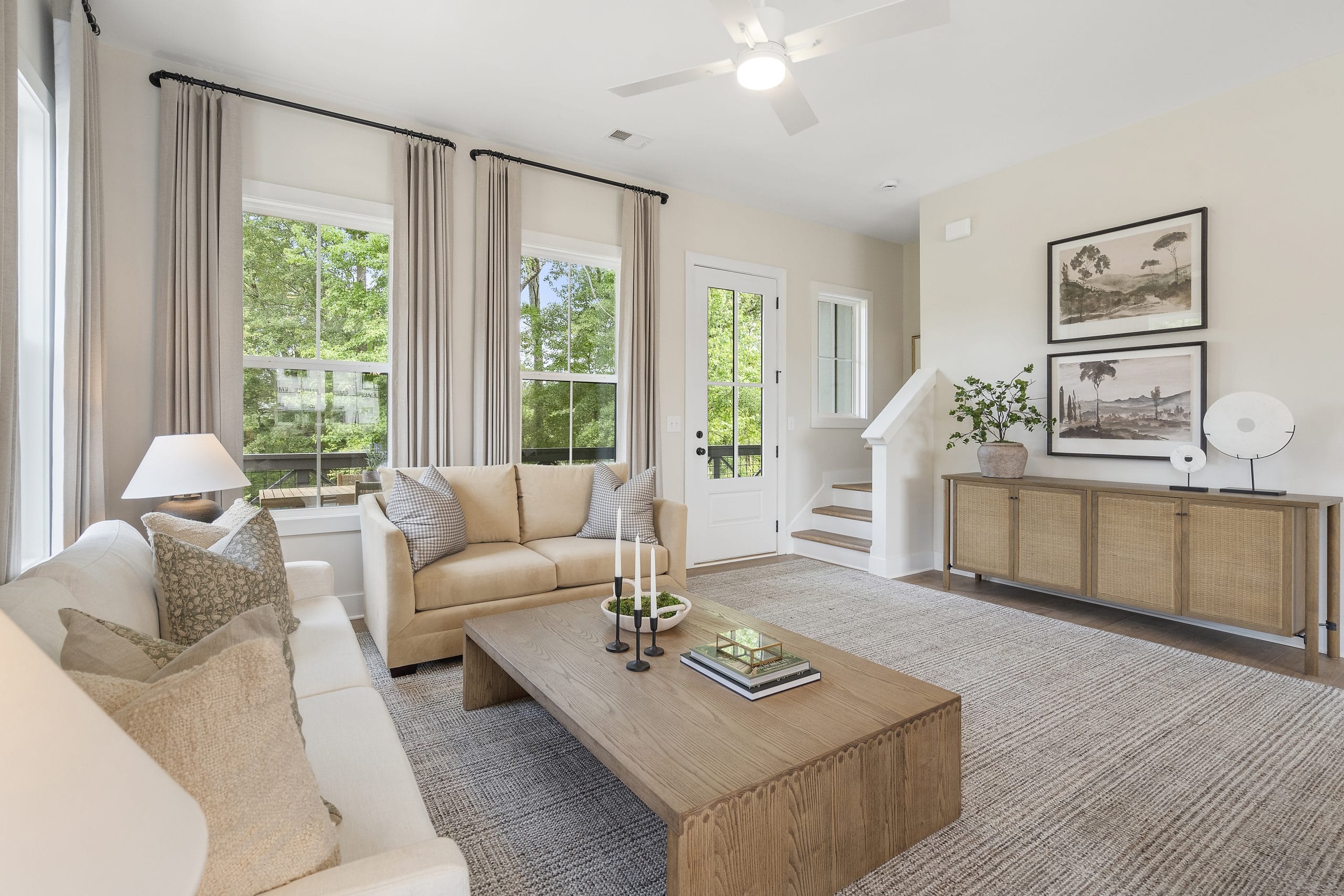 Bright living room with beige furniture, large windows, wooden coffee table, and decorative items.