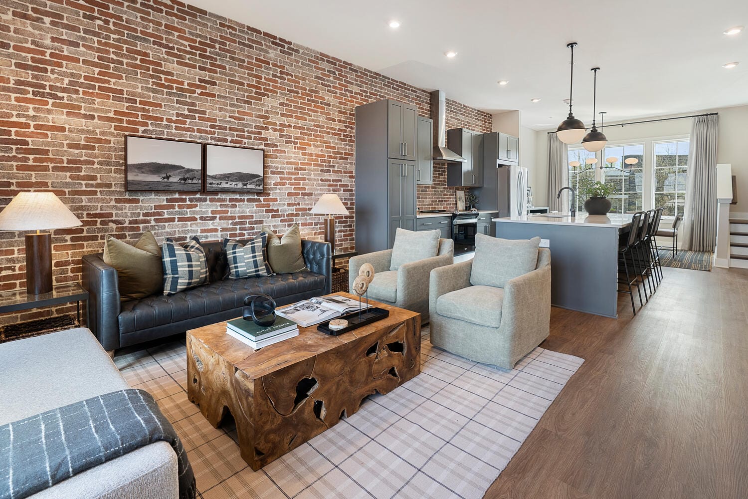 living room with dark leather sofa, plaid pillows, beige armchairs, wooden coffee table, and checkered rug.