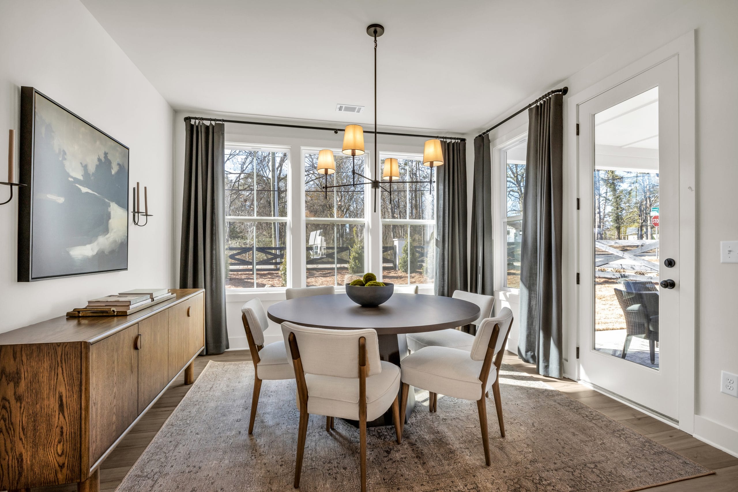 Dining room with round wooden table, upholstered chairs, and large windows.