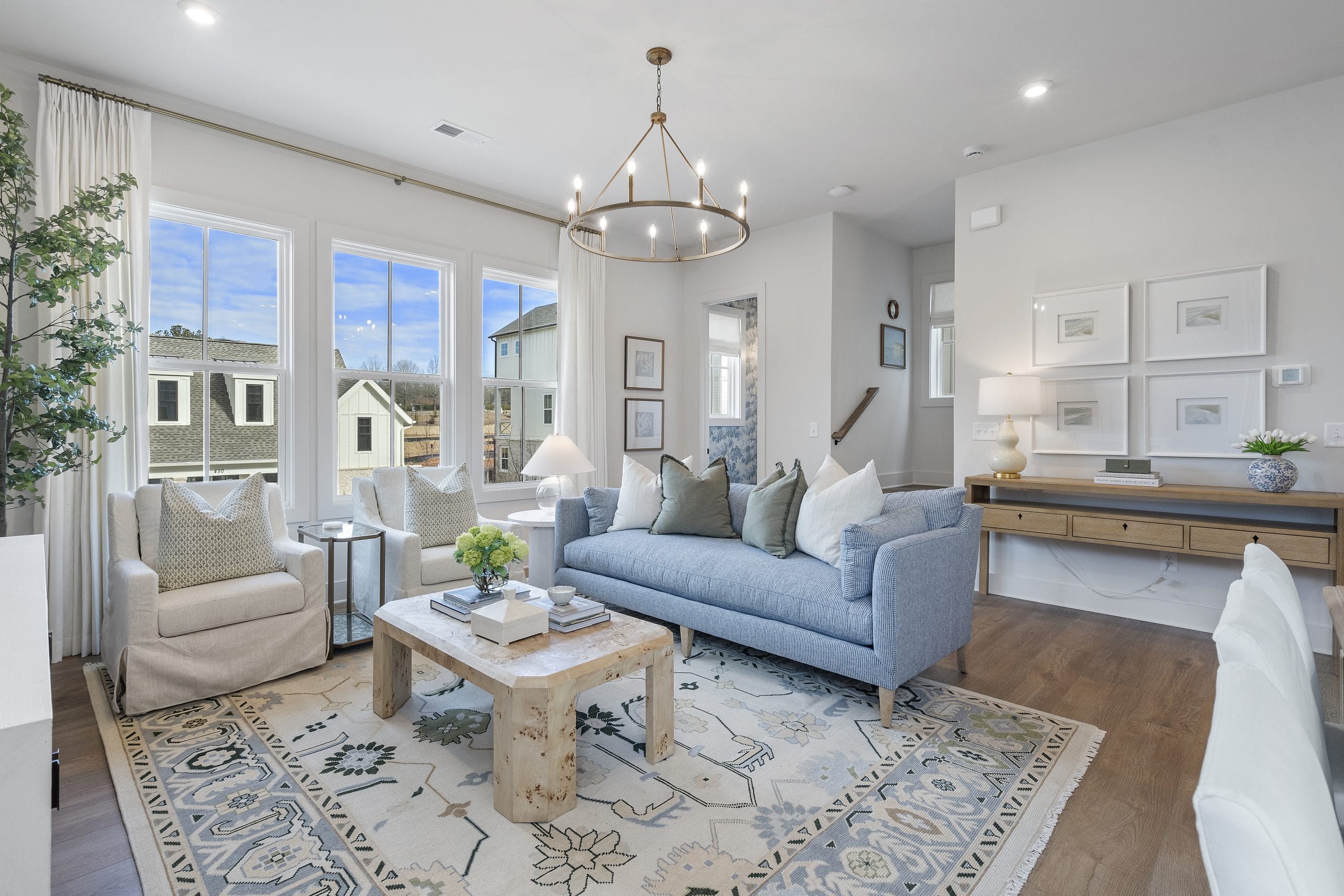 Well-decorated living room with large window, patterned rug, blue and white striped sofa, armchairs, wooden coffee table, chandelier, and framed artwork.