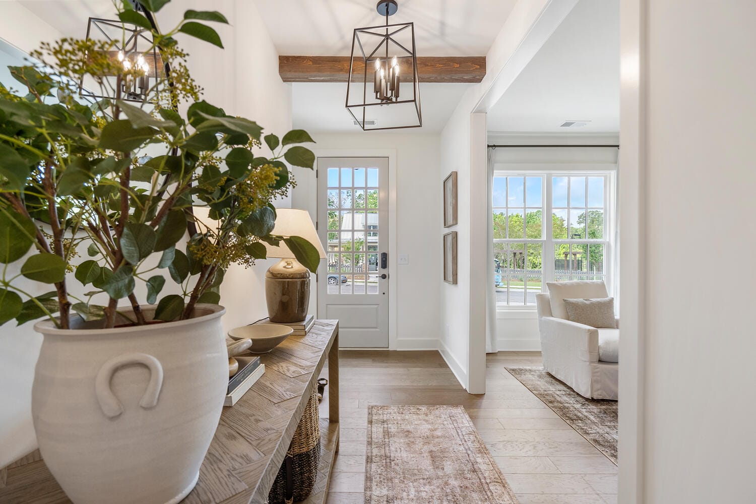 Bright hallway with potted plant on console table, pendant lights, light-colored tile floor, and front door with glass panels.