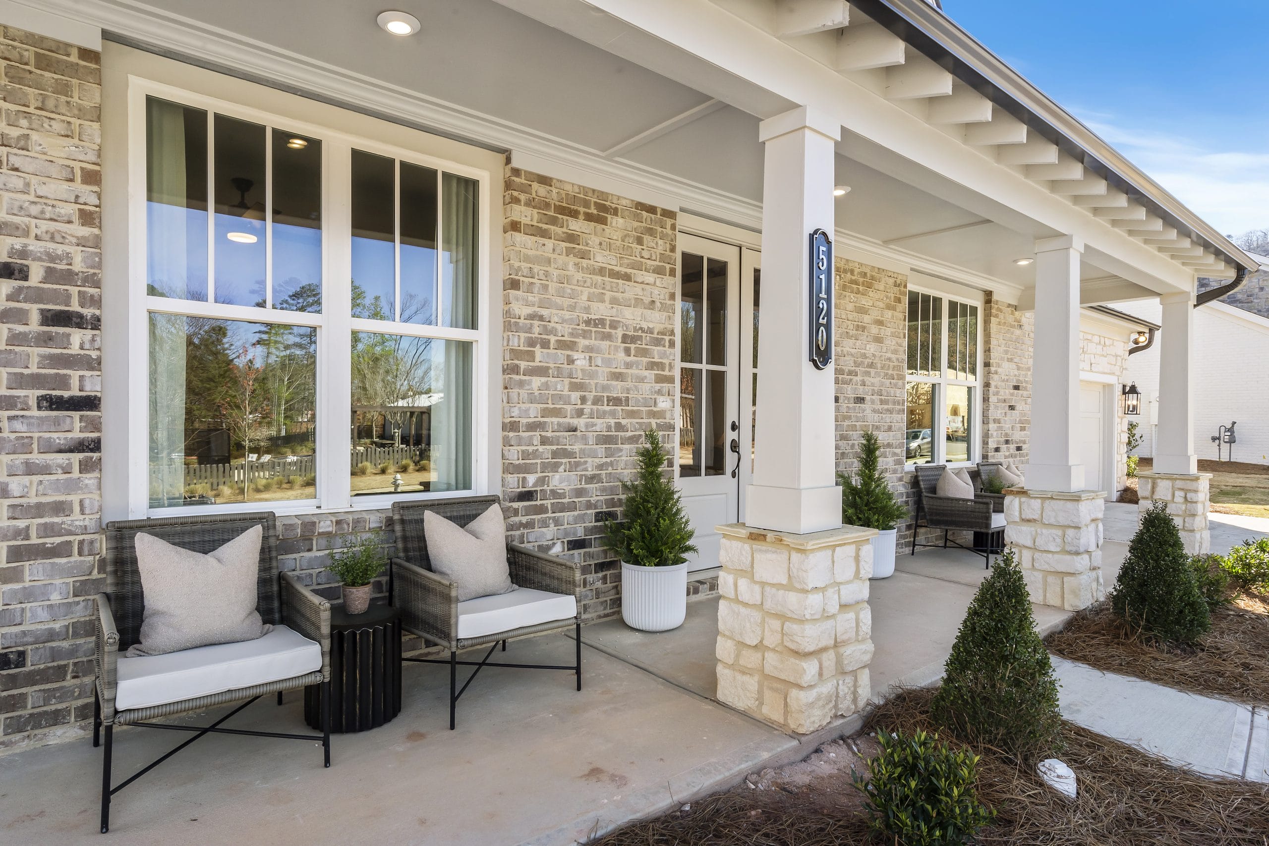 Front porch with brick walls, white trim, cushioned chairs, small table, potted plants, house number 5120.