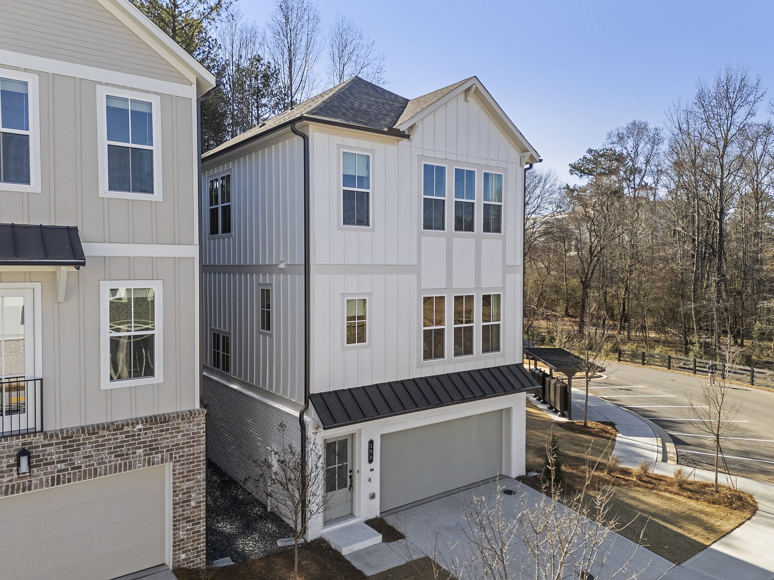 Multi-story house with light-colored exterior, large windows, garage, and trees nearby.