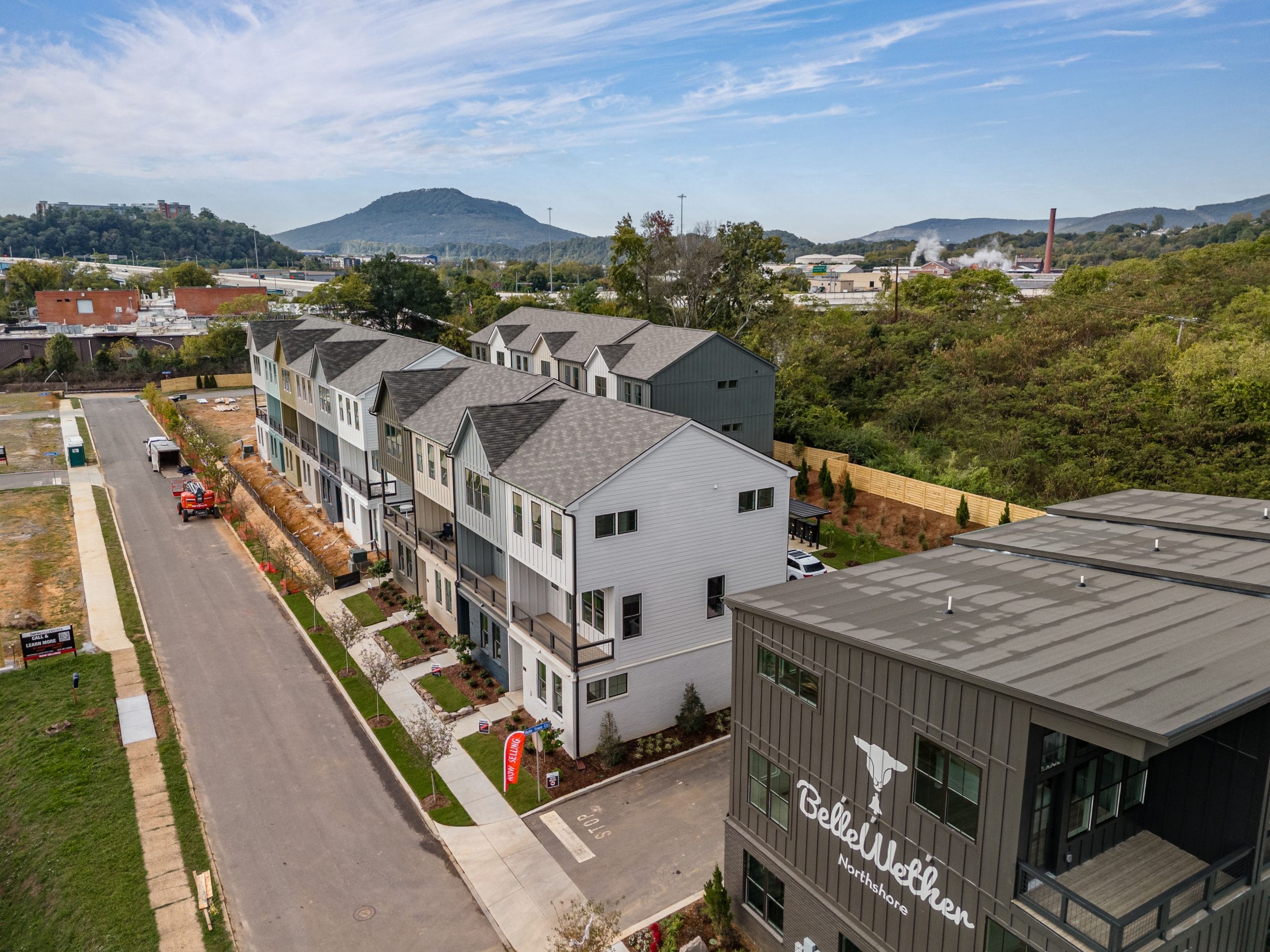Townhouses along a street with a hilly landscape and industrial structures in the background