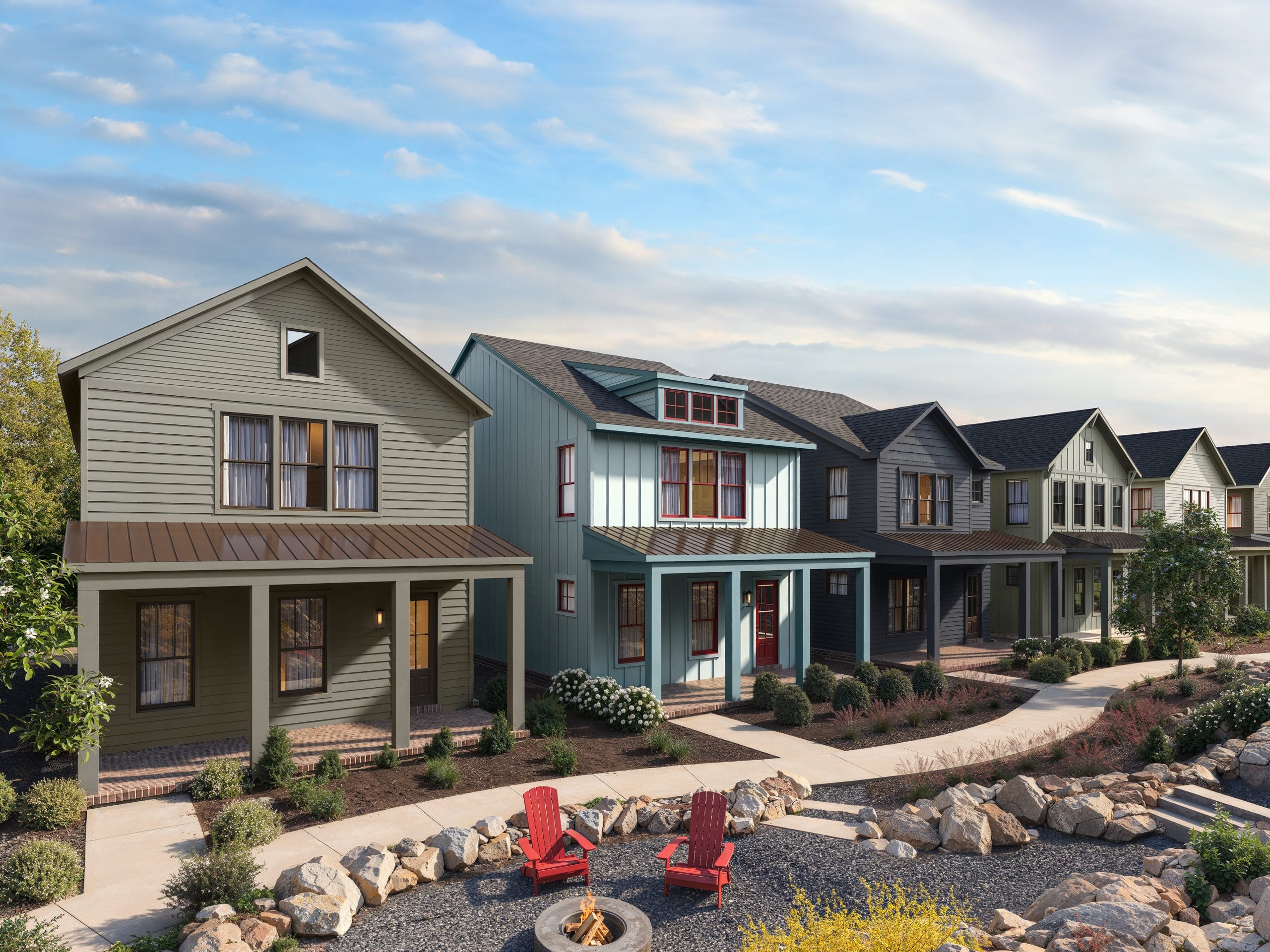 Row of modern two-story houses with various designs and colors, landscaped area with rocks, plants, fire pit, and red chairs, partly cloudy sky.